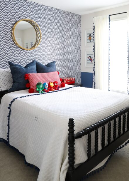 Blue and white wallpaper behind a black bed with red, white, and blue linens and superhero stuffed toys