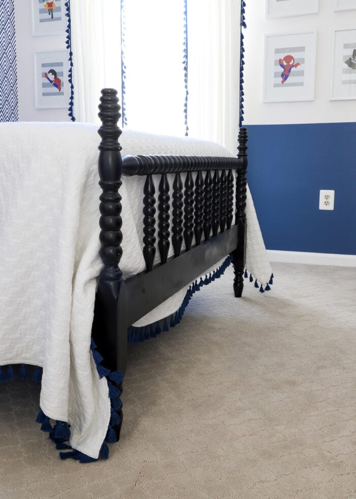 Black Jenny Lind bed with a white bedspread in a navy blue superhero-themed bedroom