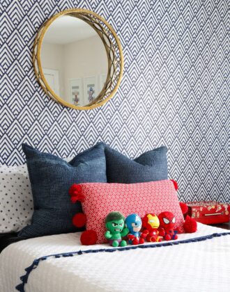 Blue and white wallpaper behind a black bed with red, white, and blue linens and superhero stuffed toys