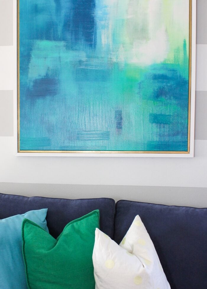 Framed canvas artwork above a blue couch on a striped wall
