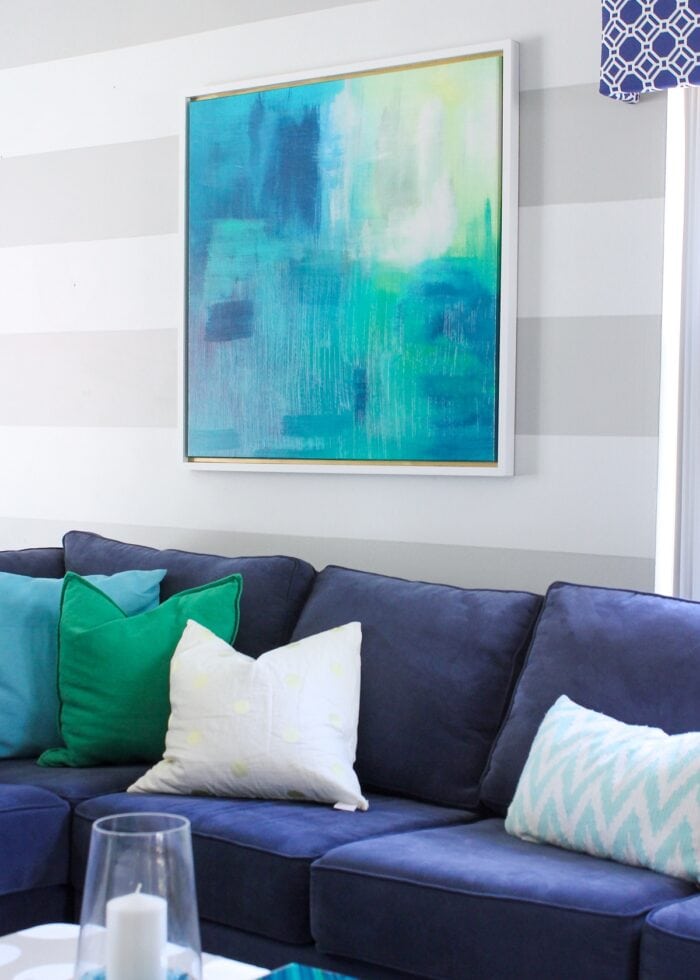 Framed canvas artwork above a blue couch on a striped wall