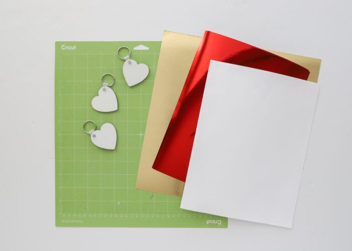 Cricut mat shown with red, gold, and white paper and three heart keychains