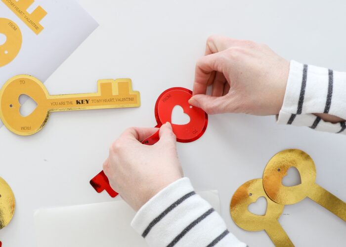 Hands sticking red Valentine key onto foil paper backing