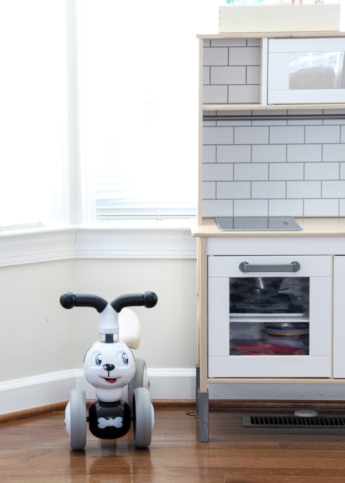 Little puppy dog bike next to a play kitchen in a playroom