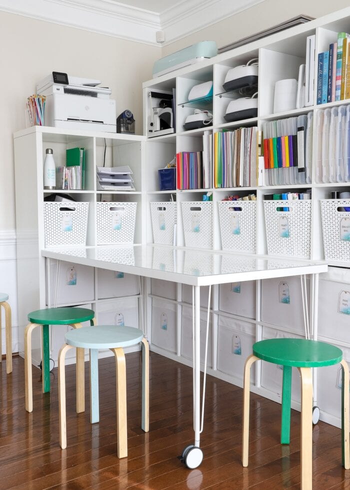 IKEA Kallax shelves loaded up with craft supplies in home office shown with table and stools