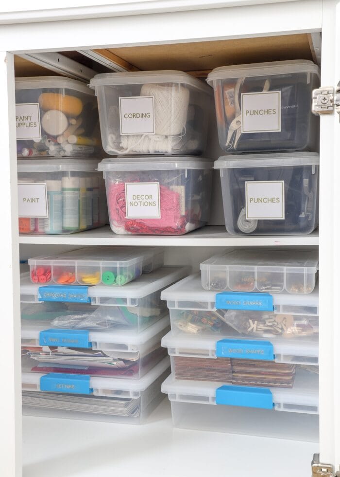 Plastic boxes holding craft supplies inside white cabinet