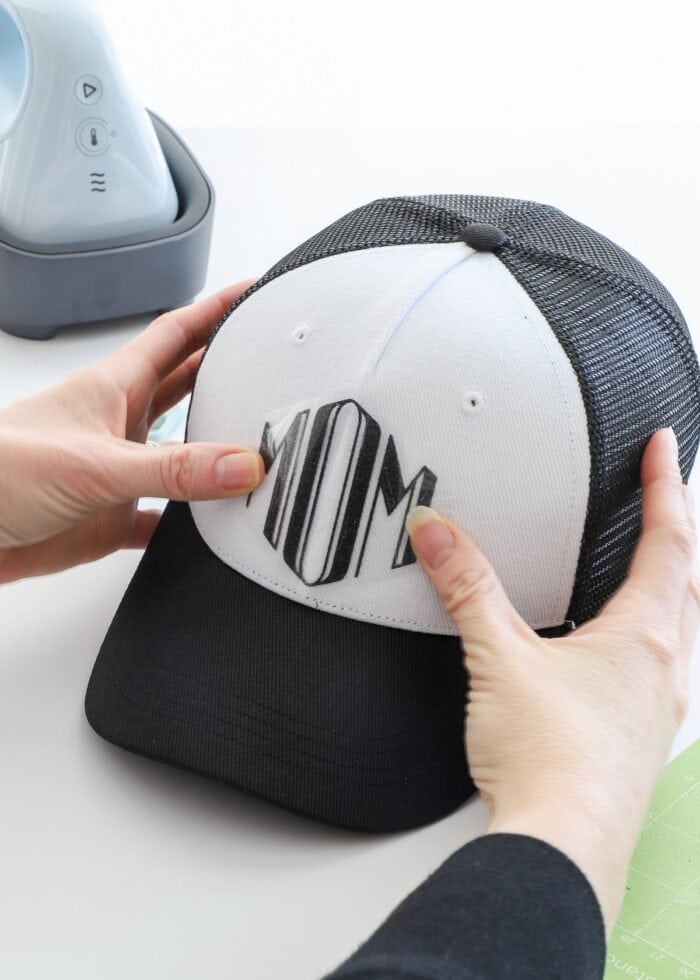 Hands placing iron-on vinyl design onto Cricut Trucker Hat