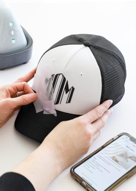 Hands removing tape from iron-on design on Cricut Trucker Hat