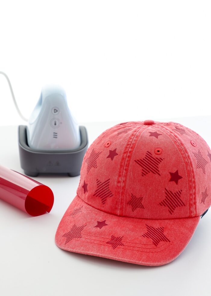 A red baseball cap with stars shown next to Cricut Hat Press