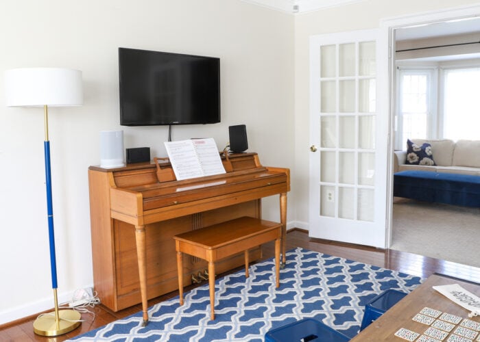Wooden piano shown with blue lamp and rug