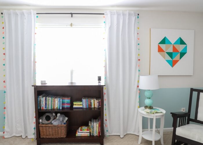 Nursery windows with white curtains and brown bookshelf underneath