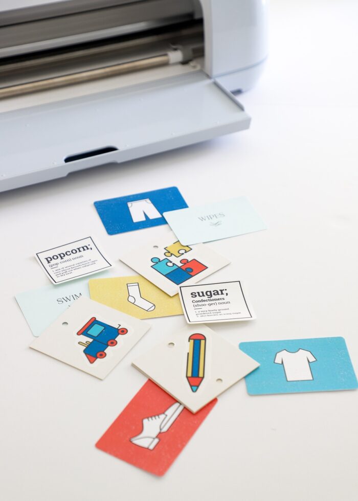 A set of colorful labels made with Cricut Print Then Cut shown alongside Cricut Maker 3