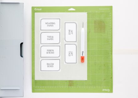Printable labels on a green cut mat sitting next to Cricut Maker 3