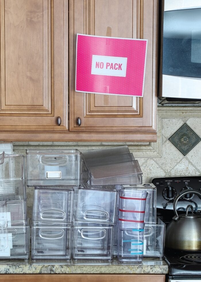 A pink "No Pack" sign on a brown cabinet with empty canisters on counter beneath
