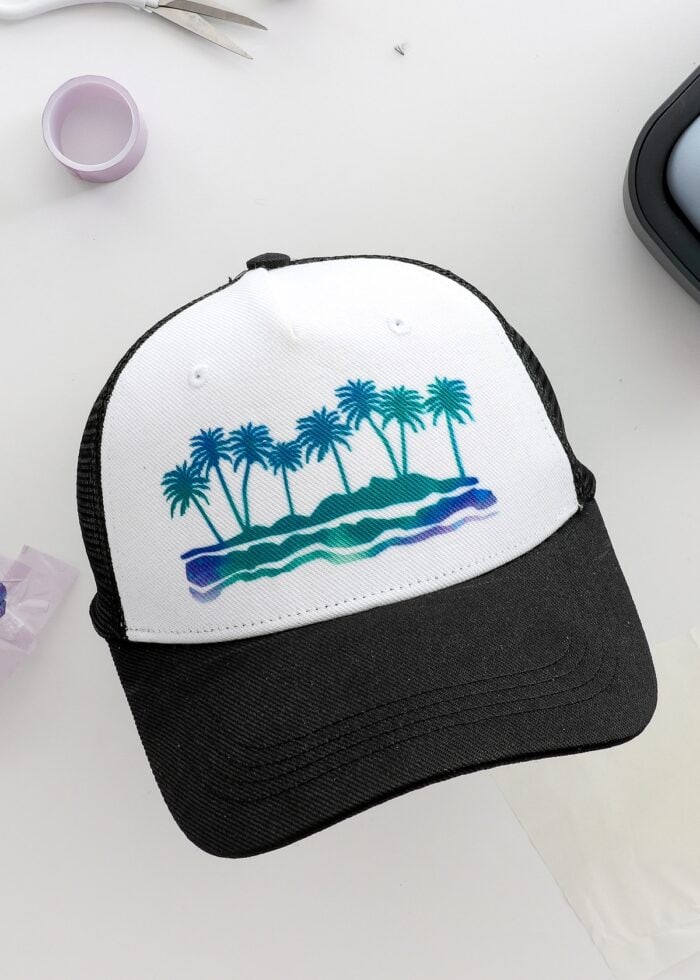 A black trucker hat with an Infusible Ink design of palm trees
