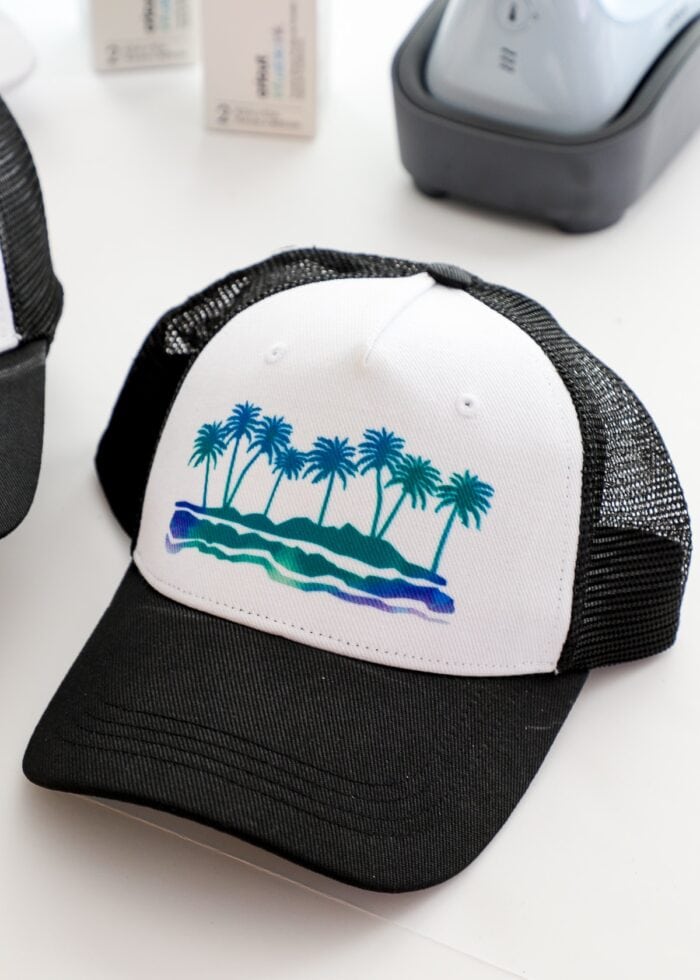 A black trucker hat with an Infusible Ink design of palm trees