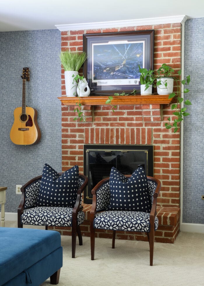 Red brick fireplace surrounding by blue wallpaper with plants on the mantel