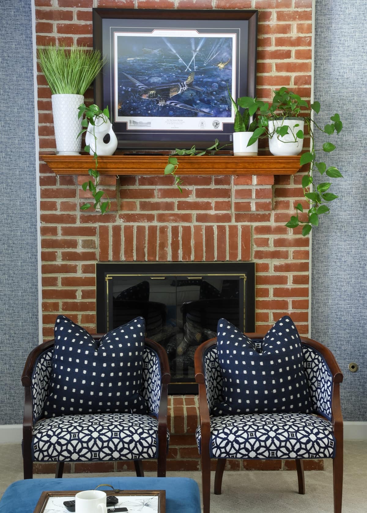 Red brick fireplace with navy blue wallpaper and patterned chairs in front