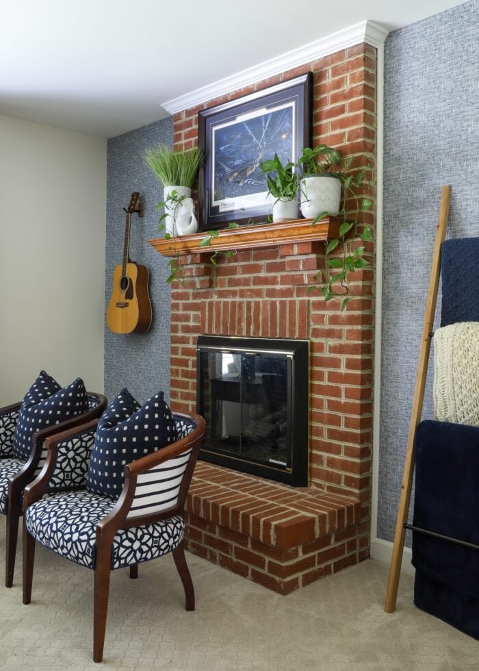 Red brick fireplace with navy blue wallpaper and patterned chairs in front