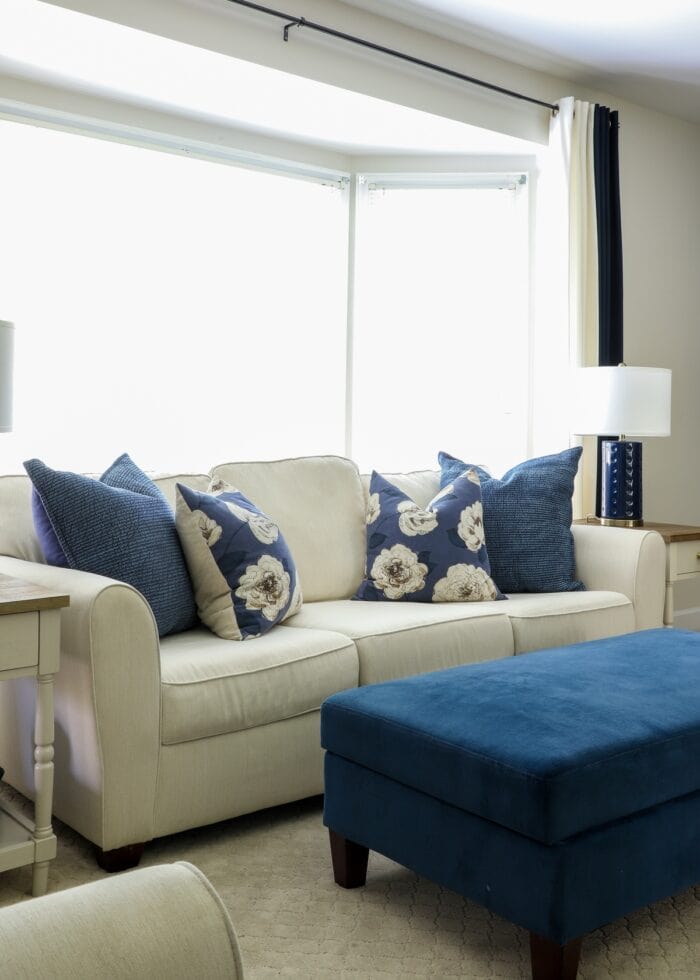 White couch sitting in a bright bay window with a blue ottoman in front