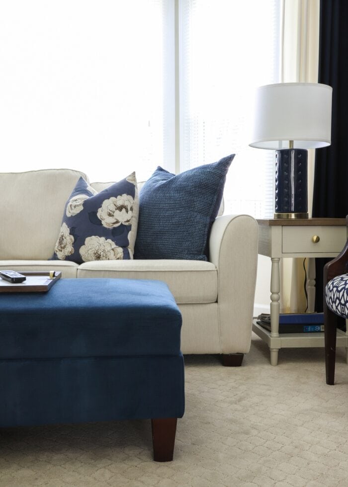 White couch sitting in a bright bay window with a blue ottoman in front