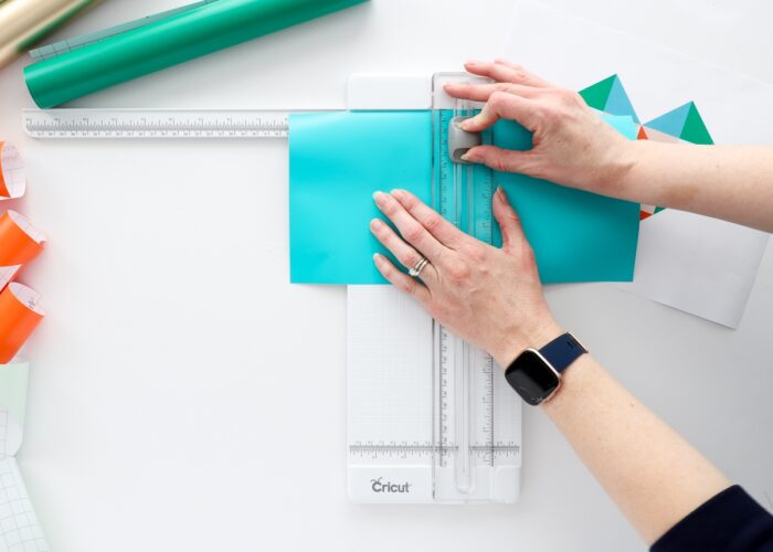 Hands cutting a turquoise piece of vinyl with a Cricut Paper Trimmer