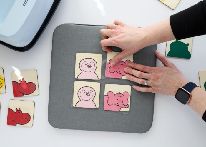 Hands placing a black outline layer of iron-on vinyl onto DIY Memory Game tiles