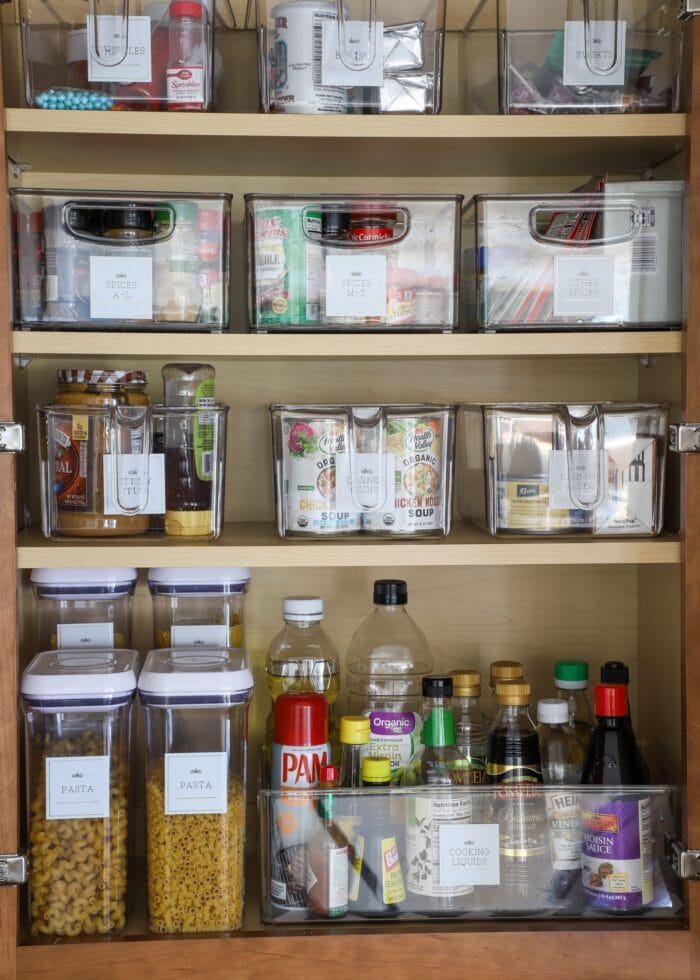 Kitchen cabinet filled with clear bins holding pantry items