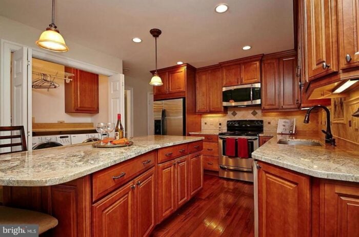 Rental kitchen with wood cabinets and rustic tile backsplash and laundry room doors open