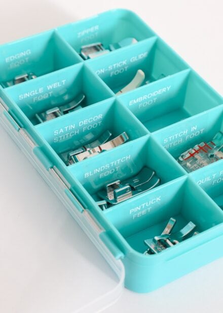 Turquoise box holding sewing machine feet labeled with white letters