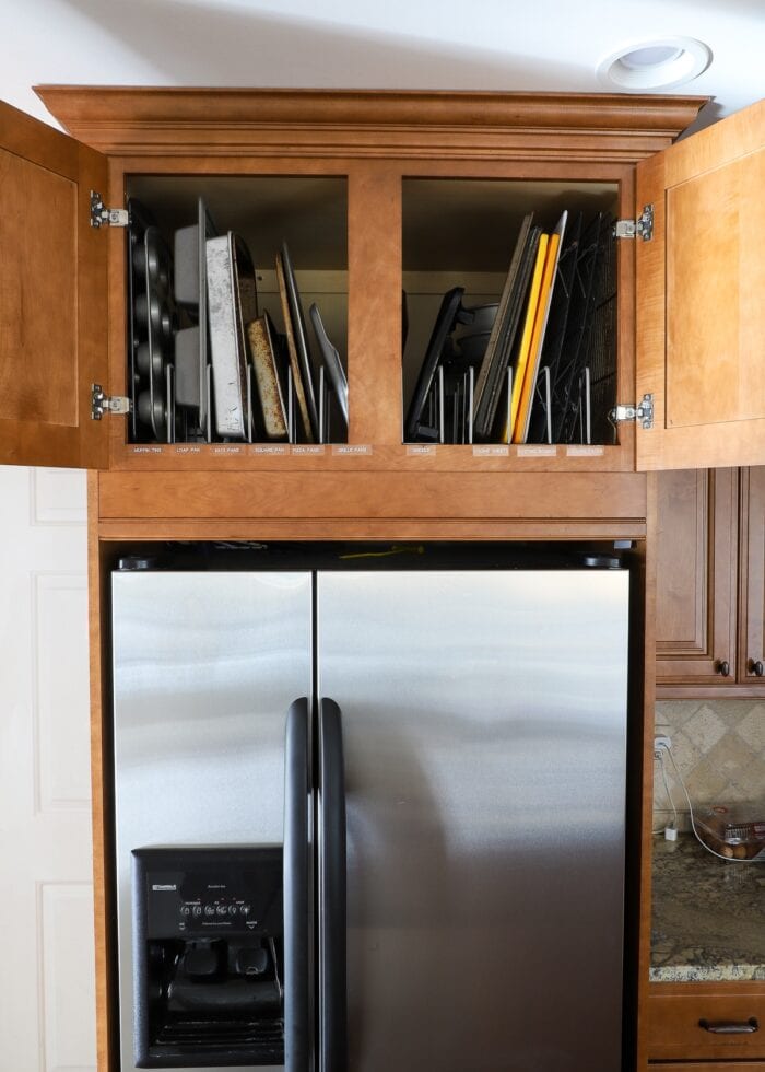 Cabinets above the refrigerator holding baking pans