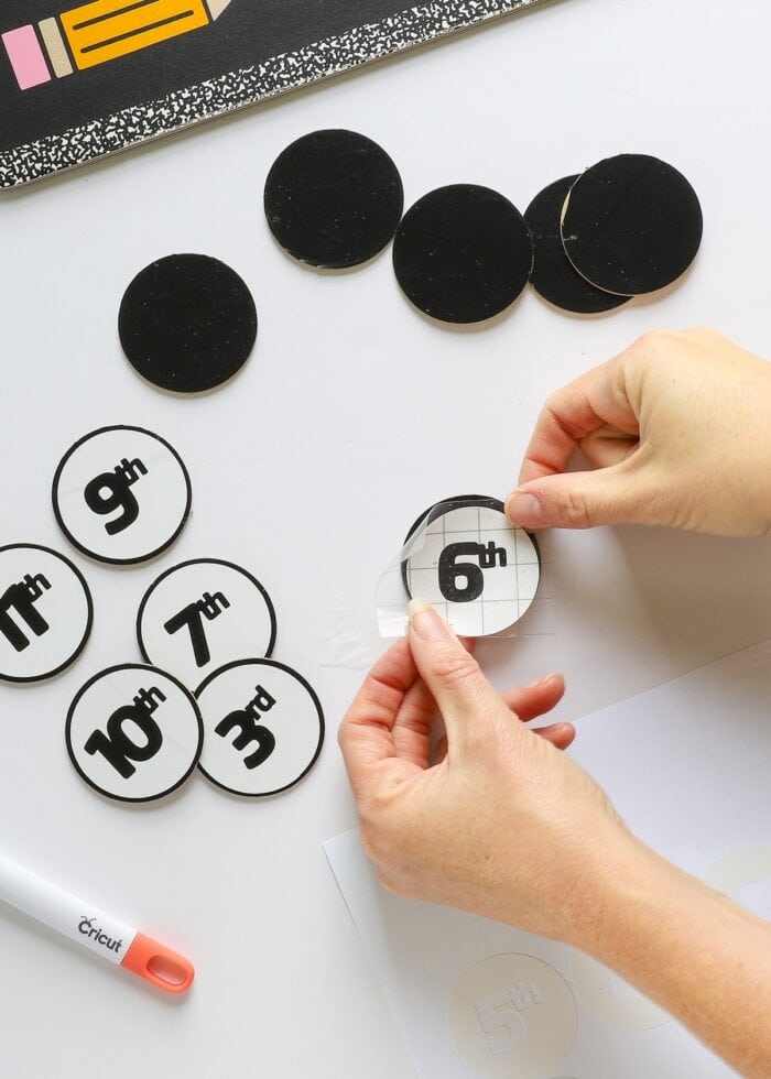 Hands placing vinyl numbers onto chipboard circles
