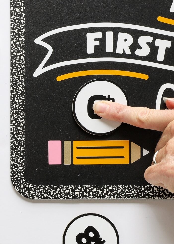 Finger placing grade onto first day of school sign