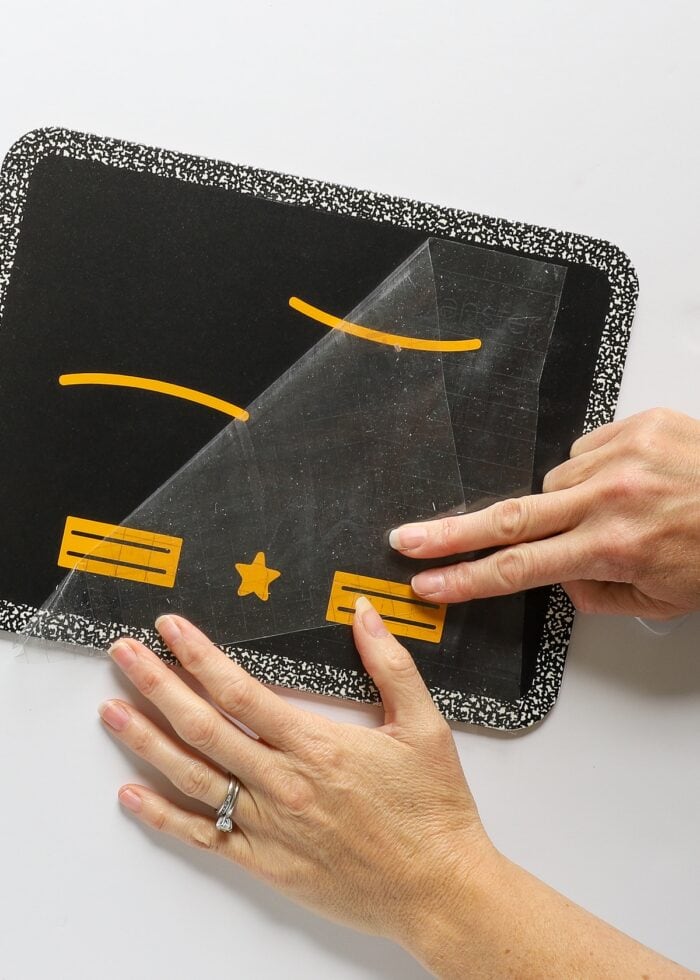 Hands transferring yellow vinyl design onto chalkboard