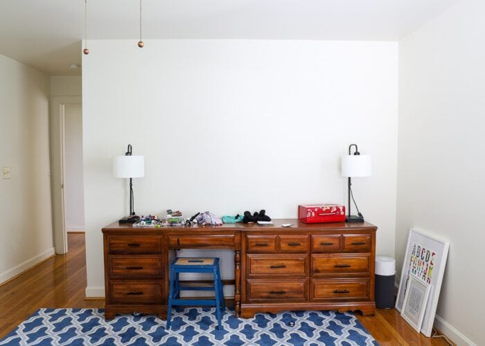 White wall of bedroom with brown dressers and blue carpet