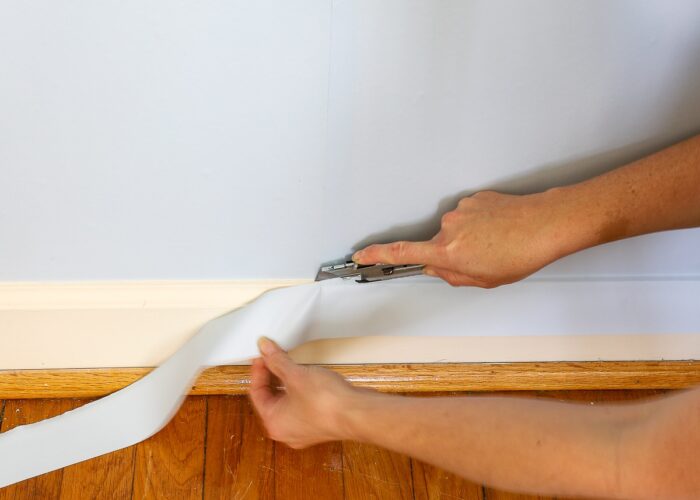 Hand using sharp blade to cut away excess wallpaper mural
