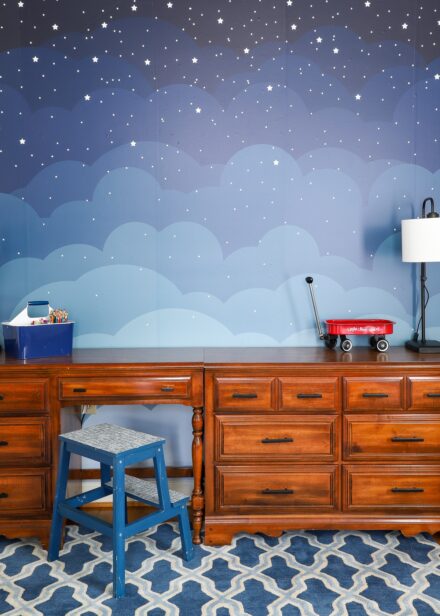 Gorgeous blue cloud mural behind brown dressers in child's bedroom