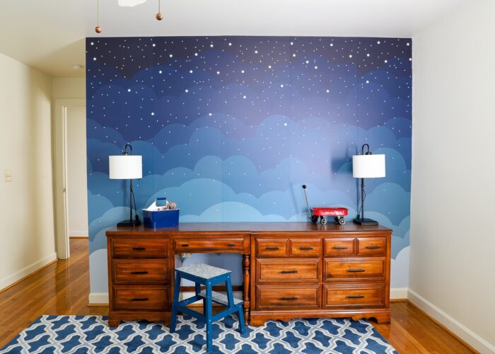 Gorgeous blue cloud mural behind brown dressers in child's bedroom