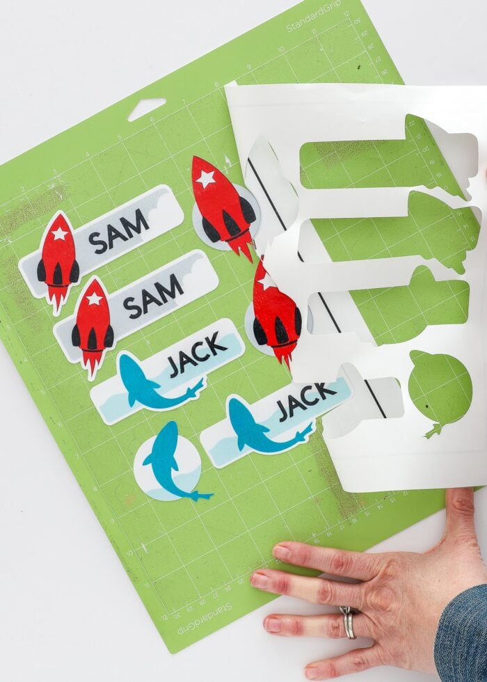Hands pulling away excess sticker paper from around cut waterproof stickers