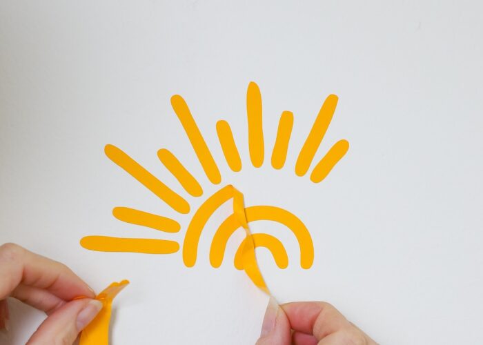 Hands peeling off vinyl sunshine decal from wall