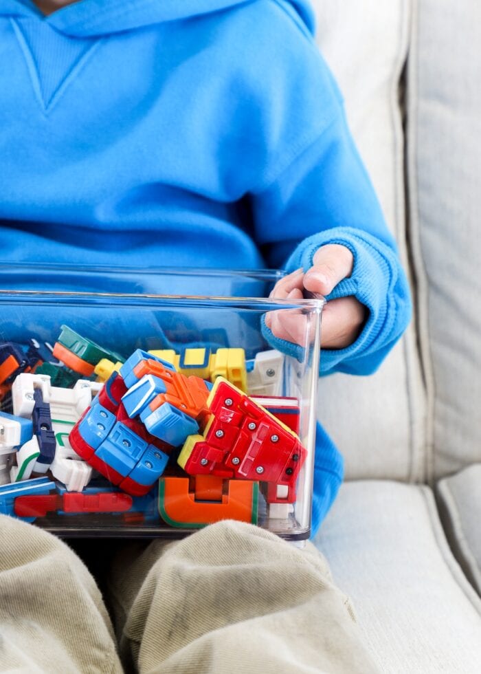 Child's hands holding clear acrylic bin full of small toys
