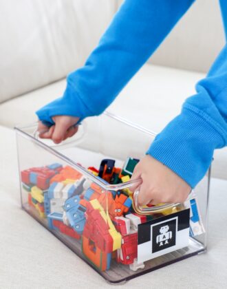 Child's hands holding clear acrylic bin full of small toys