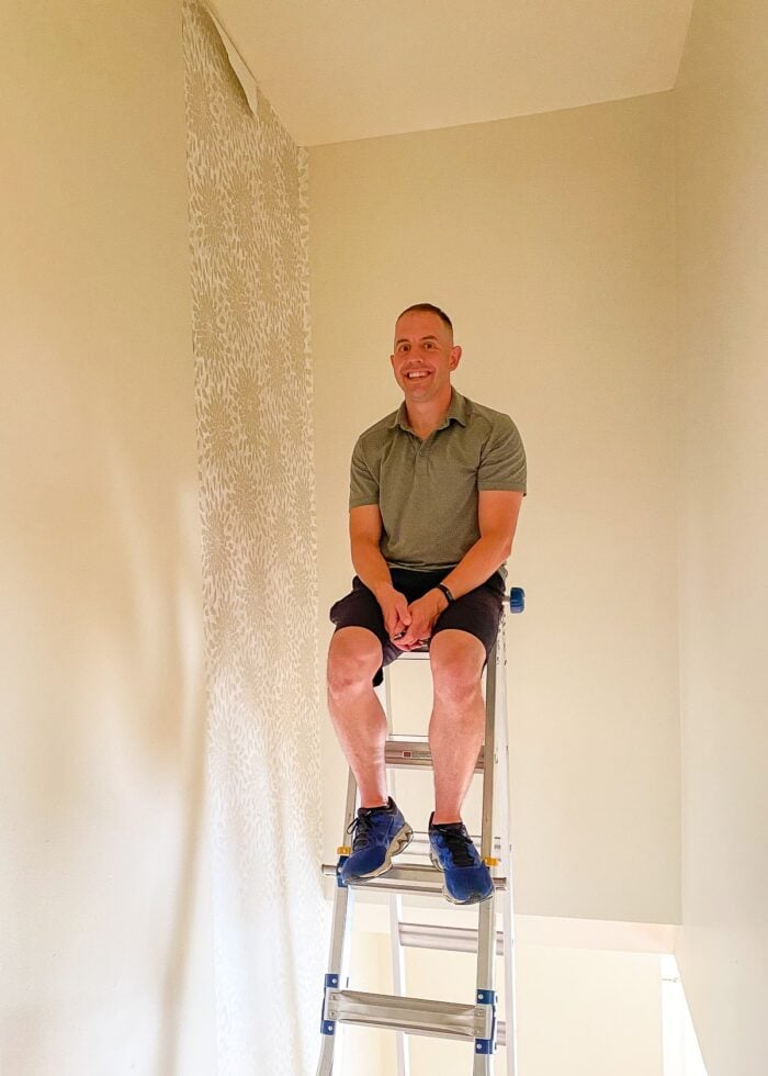Greg sitting on extension ladder in stairwell to hang wallpaper