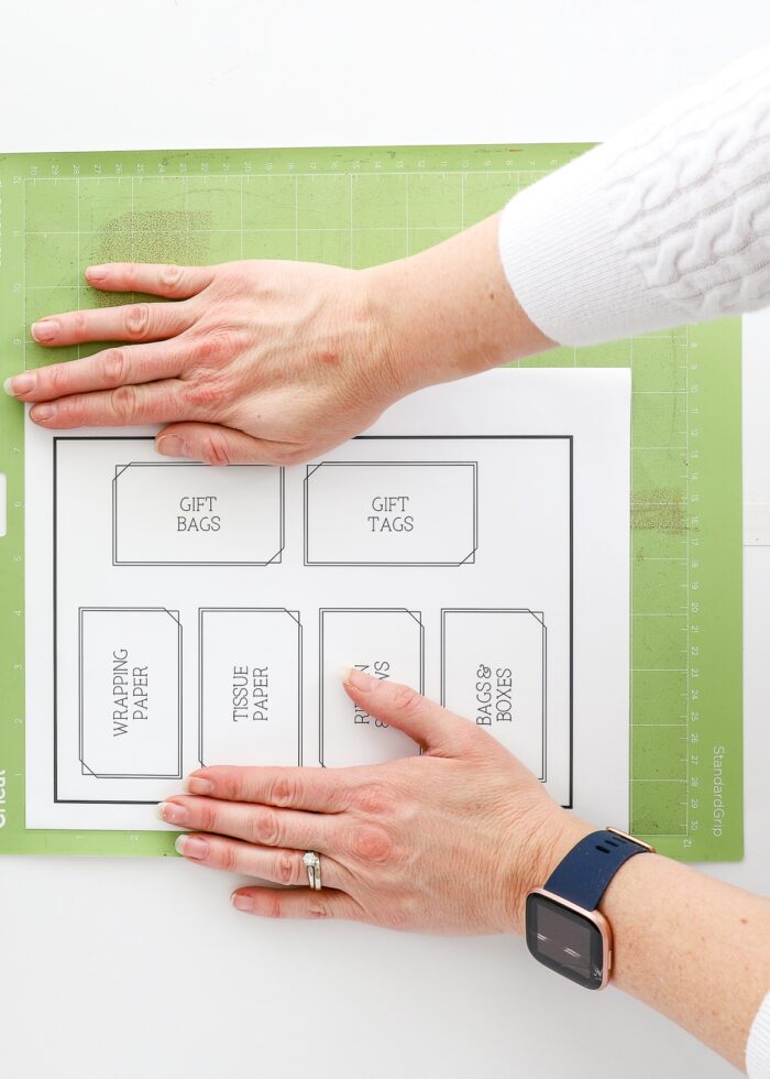 Hands placing printed labels onto a green Cricut mat