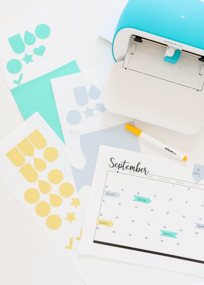 Blue, yellow, and green stickers shown next to a calendar and Cricut Joy