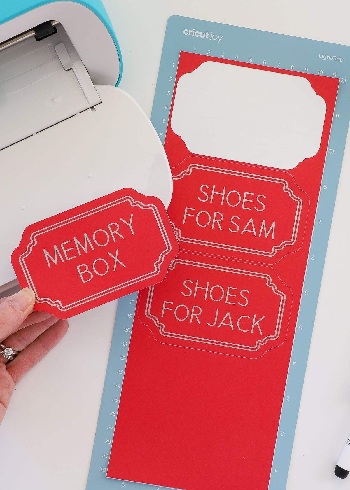 Hand holding red labels next to Cricut Joy
