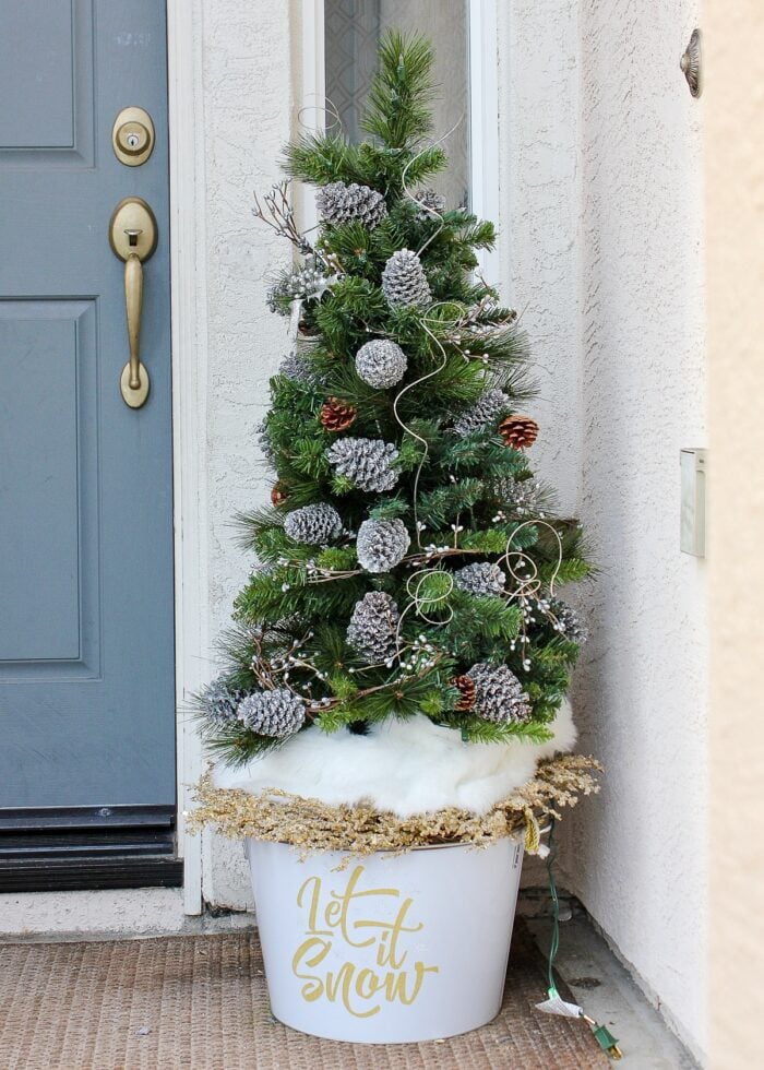 Outdoor Christmas tree in a white bucket decorated with silver pinecones