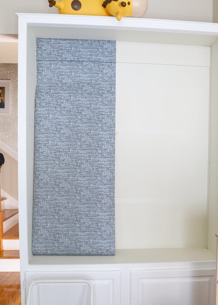 Blue peel and stick wallpaper being hung inside white bookcase
