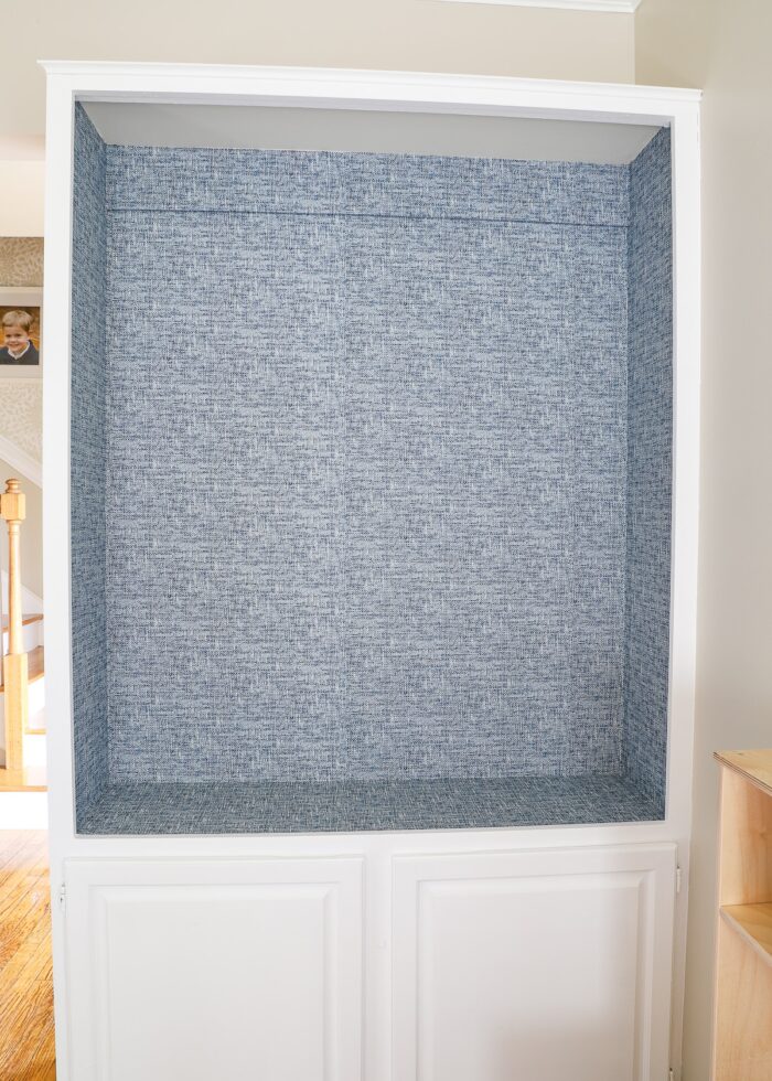 Navy poplin wallpaper lining the back of a white built-in bookcase