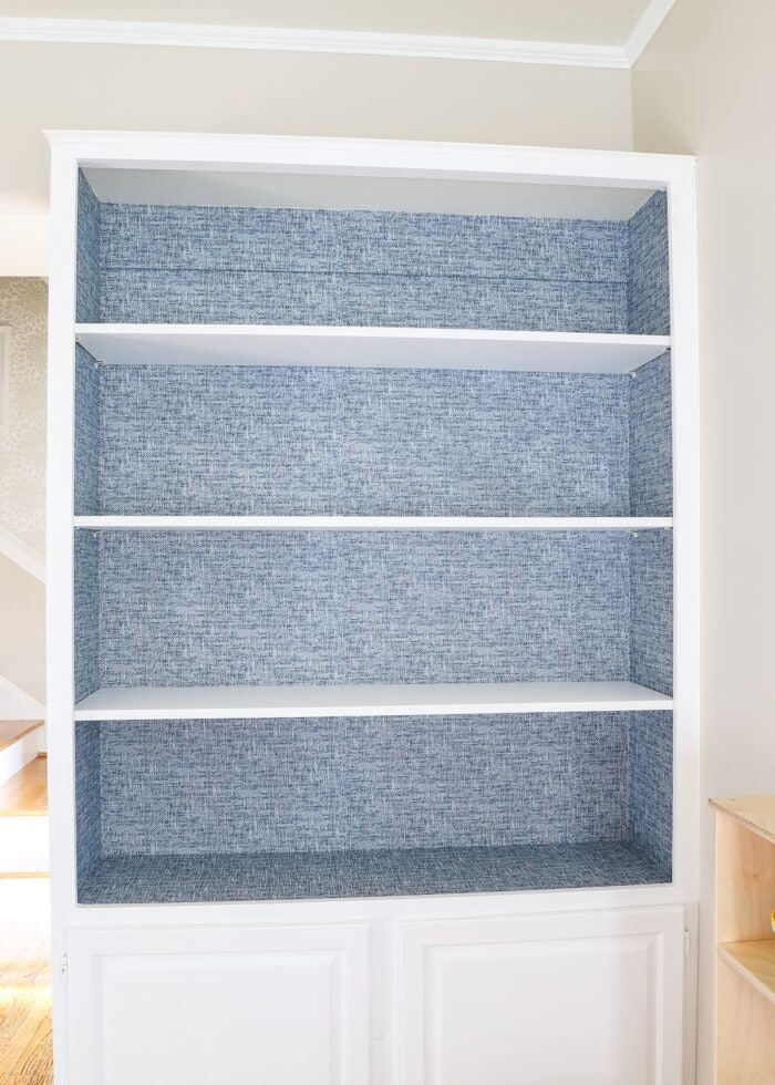 Bookshelf lined with blue wallpaper with all shelves put back in